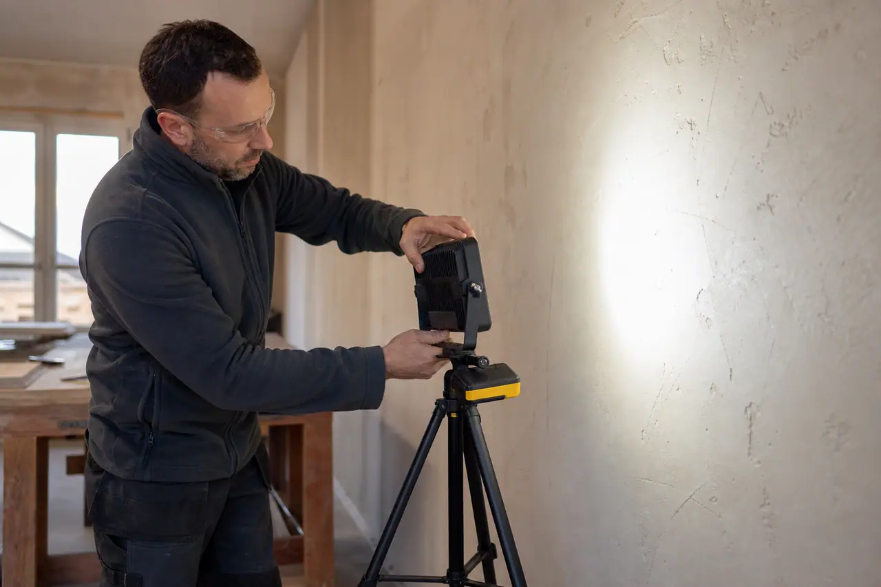 Projecteur sans fil sur trépied éclairant latéralement un mur en rénovation.