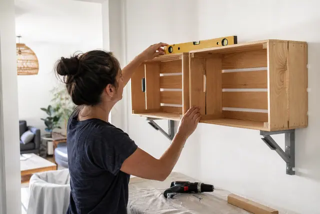 Personne fixant une étagère en caisses de bois récupérées dans un salon.