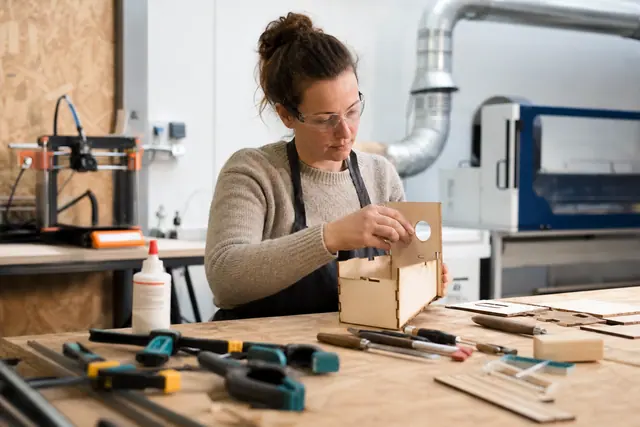 Bricoleuse assemblant un prototype en contreplaqué dans un atelier partagé équipé.