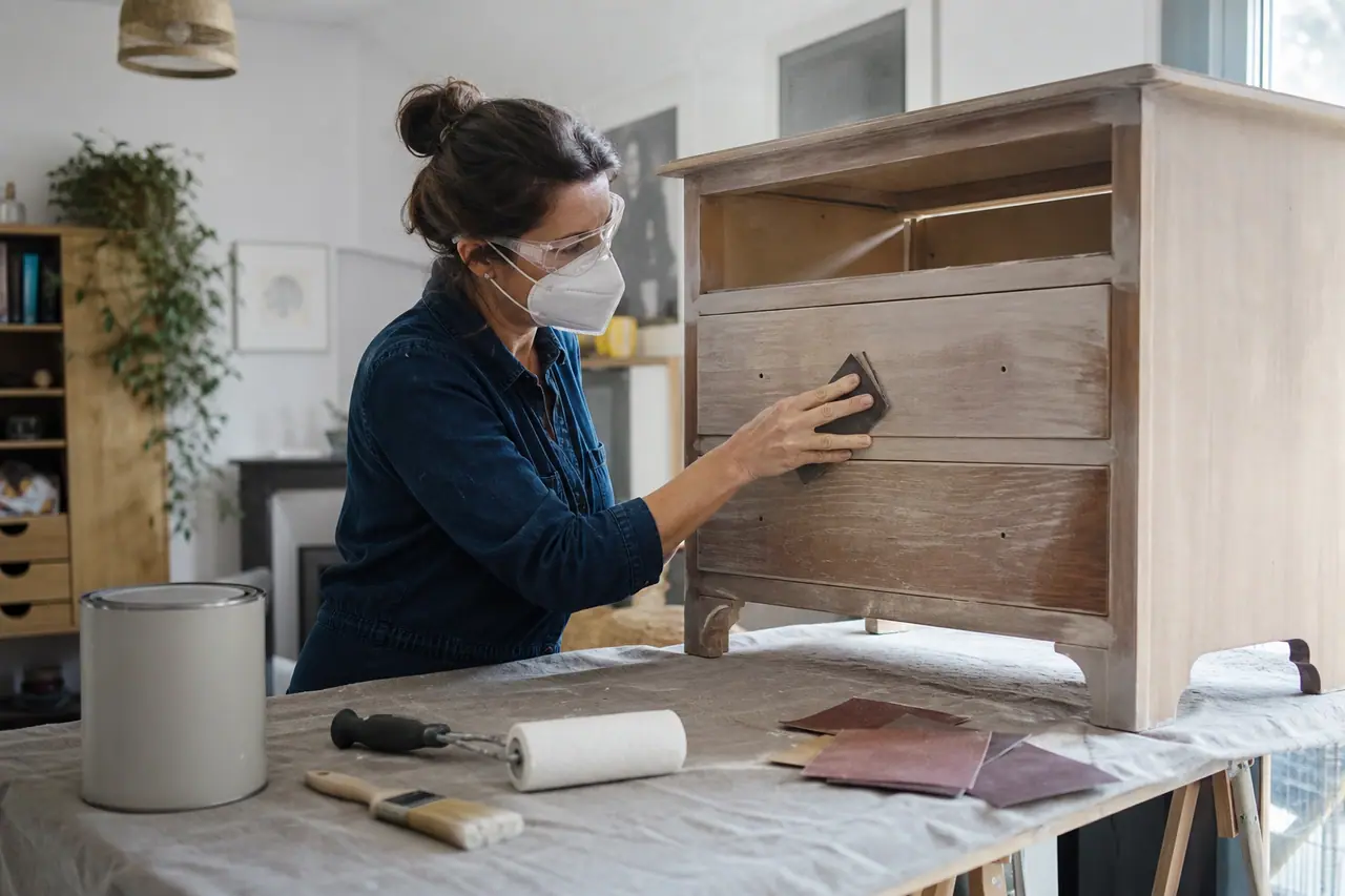 Débutante préparant une petite commode avant de la repeindre dans un atelier domestique.