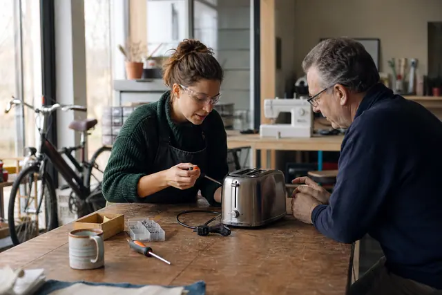 Bénévole et habitant diagnostiquant un petit appareil débranché dans un atelier partagé.