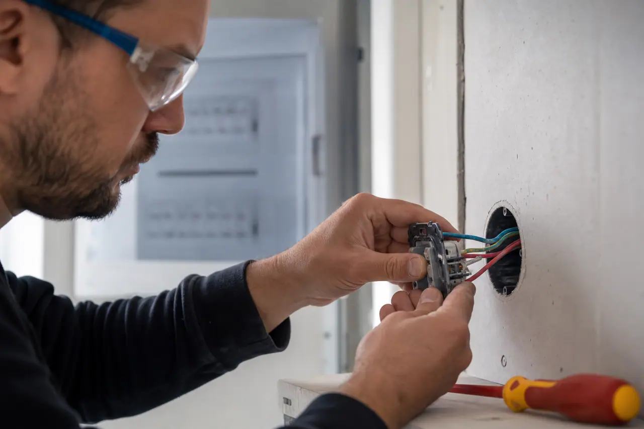 Bricoleur raccordant une prise encastrée après coupure électrique sécurisée.