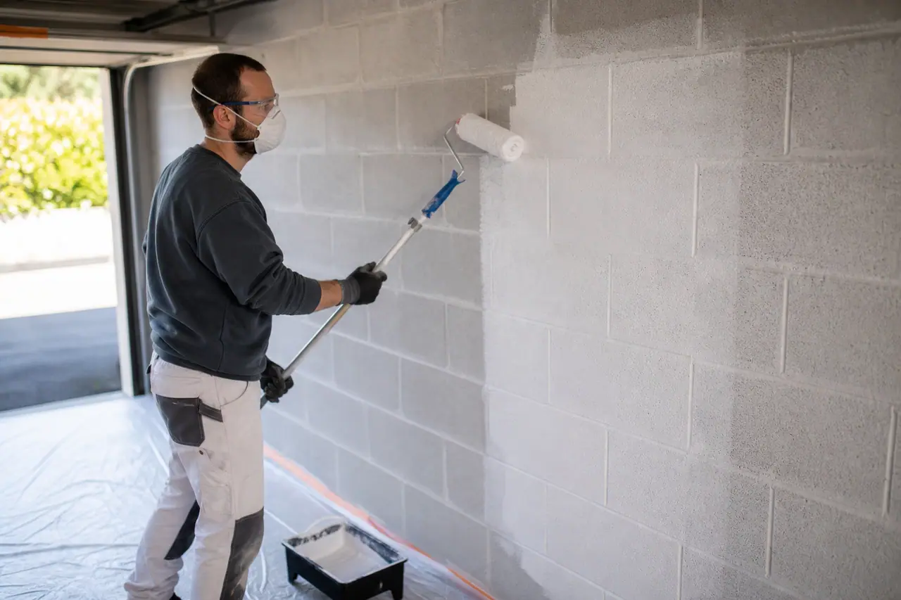 Application d’une sous-couche blanche au rouleau sur un mur intérieur en parpaings.