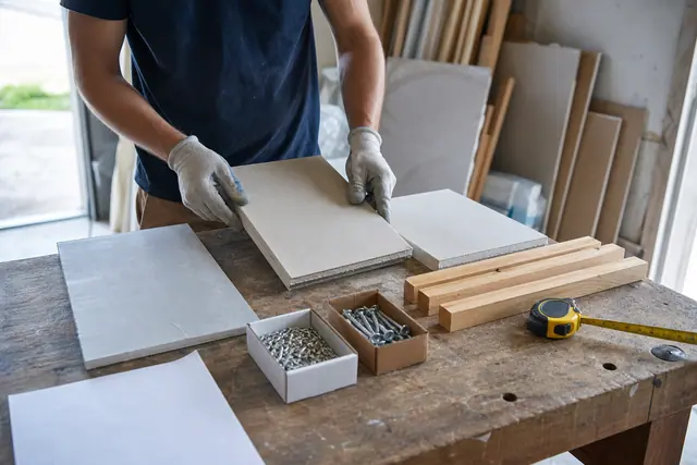 Particulier comparant des matériaux de rénovation sur un établi avec un mètre ruban.