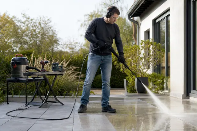 Particulier équipé nettoyant prudemment une terrasse en dalles avec un nettoyeur.