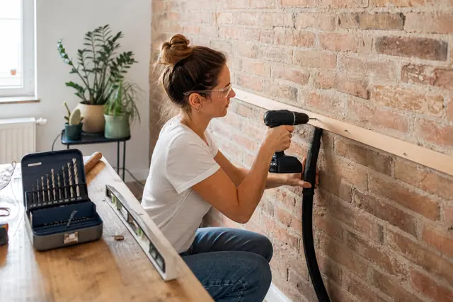 Bricoleuse équipée perce un mur en brique avec une visseuse sans fil.