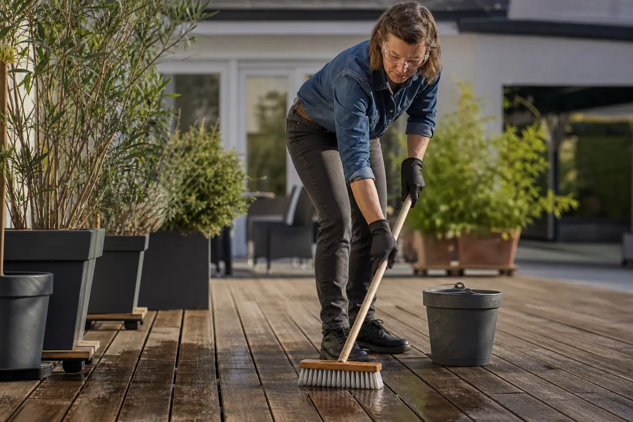 Personne brossant une terrasse en bois avec équipement de protection adapté.
