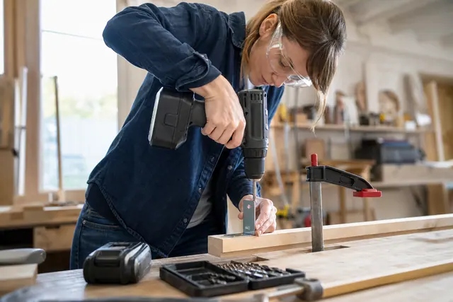 Bricoleuse équipée utilisant une perceuse-visseuse sans fil sur un tasseau fixé.