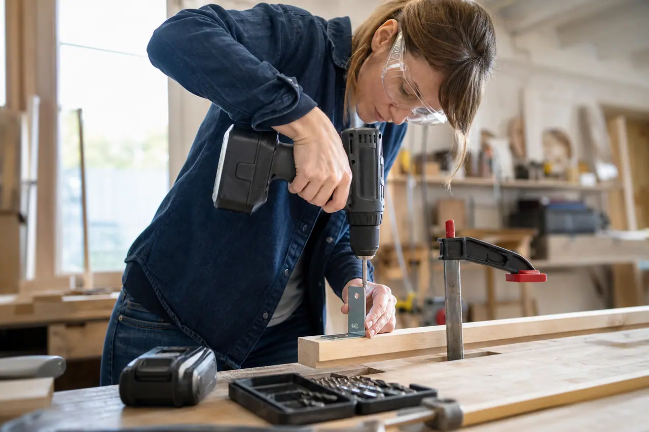 Bricoleuse équipée utilisant une perceuse-visseuse sans fil sur un tasseau fixé.