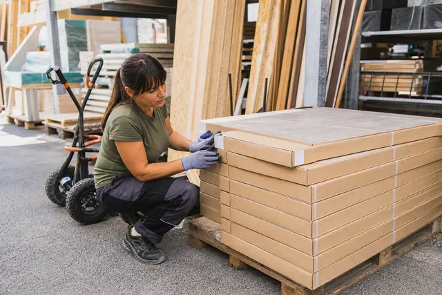 Bricoleuse contrôlant des cartons de carrelage sur une palette de déstockage.