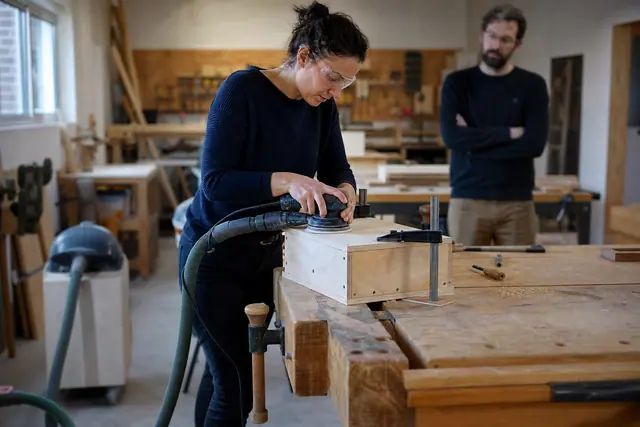 Débutante ponçant une caisse en bois dans un atelier partagé sécurisé.