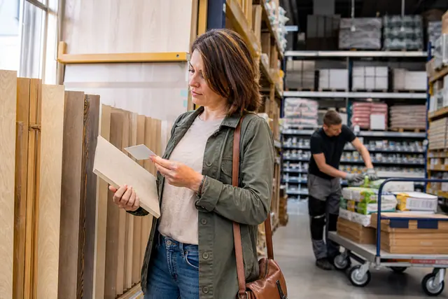 Bricoleuse comparant un panneau de bois dans un rayon matériaux bien rangé.