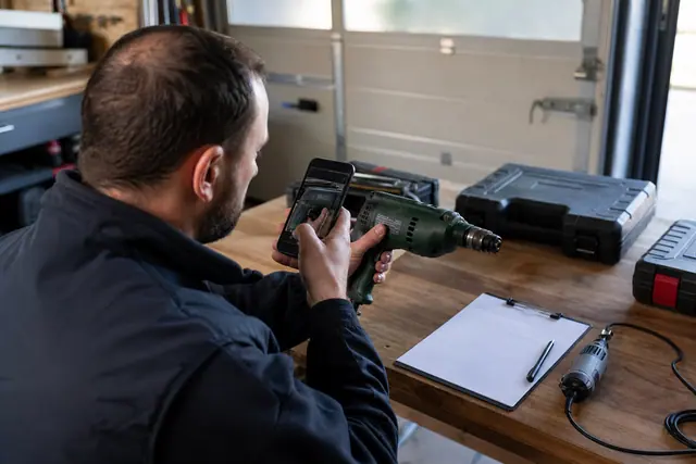 Particulier photographiant le numéro de série d’une perceuse dans son garage.