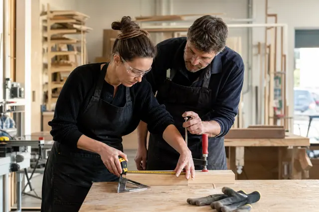 Débutante encadrée mesurant une planche dans un atelier de bricolage sécurisé.