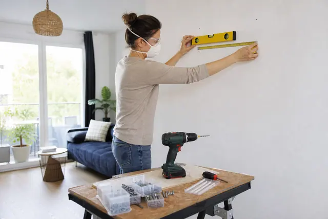 Débutante mesurant un mur avant de fixer une petite étagère.