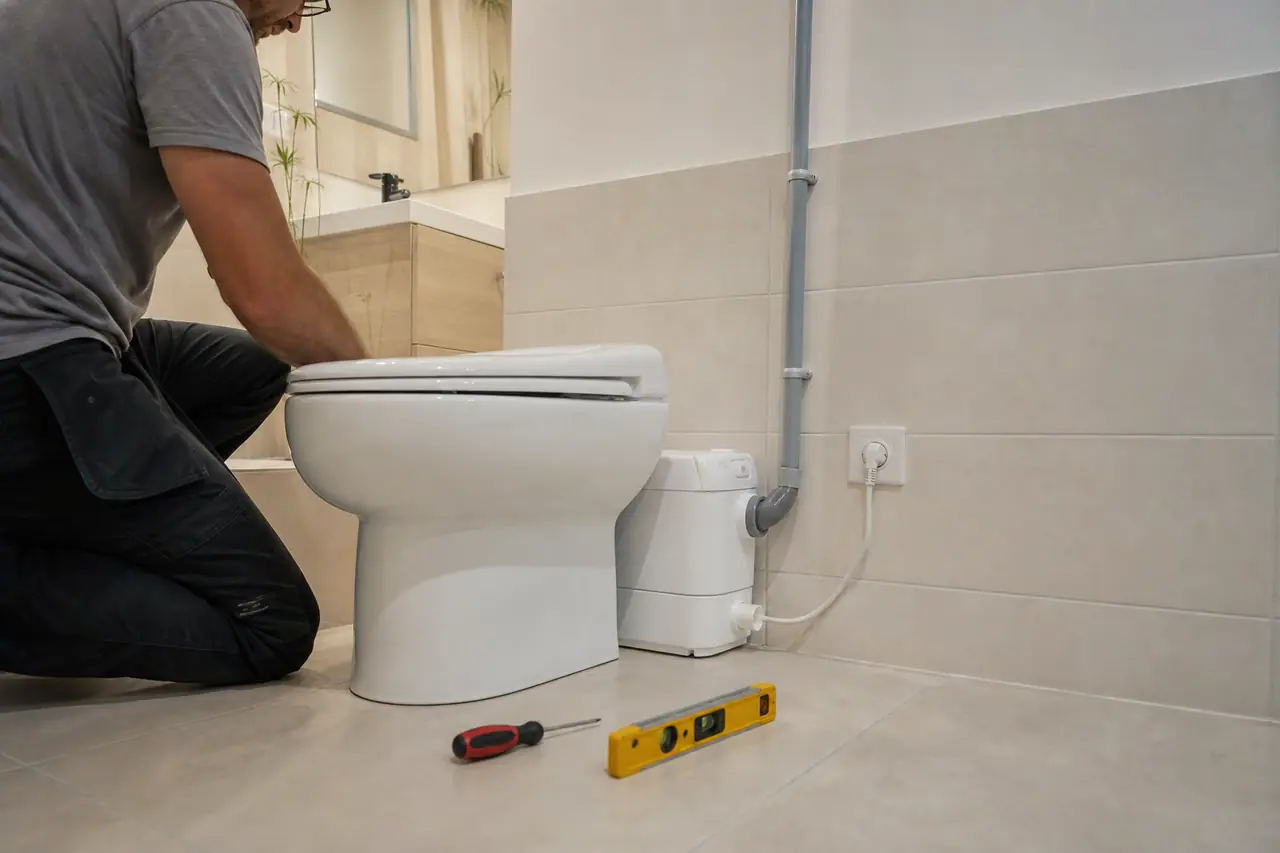 Broyeur sanitaire blanc raccordé derrière des toilettes avec canalisation de refoulement