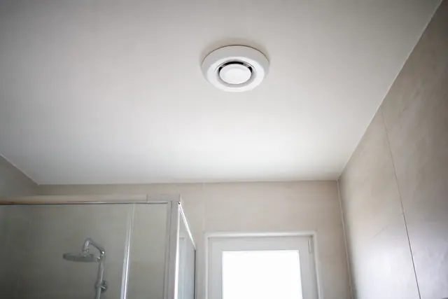 Extracteur d'air blanc installé au plafond d'une salle de bain sans fenêtre