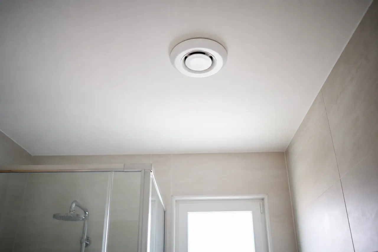 Extracteur d'air blanc installé au plafond d'une salle de bain sans fenêtre