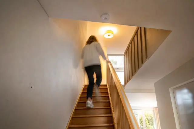 Détecteur de présence blanc fixé au plafond d'une cage d'escalier intérieure éclairée