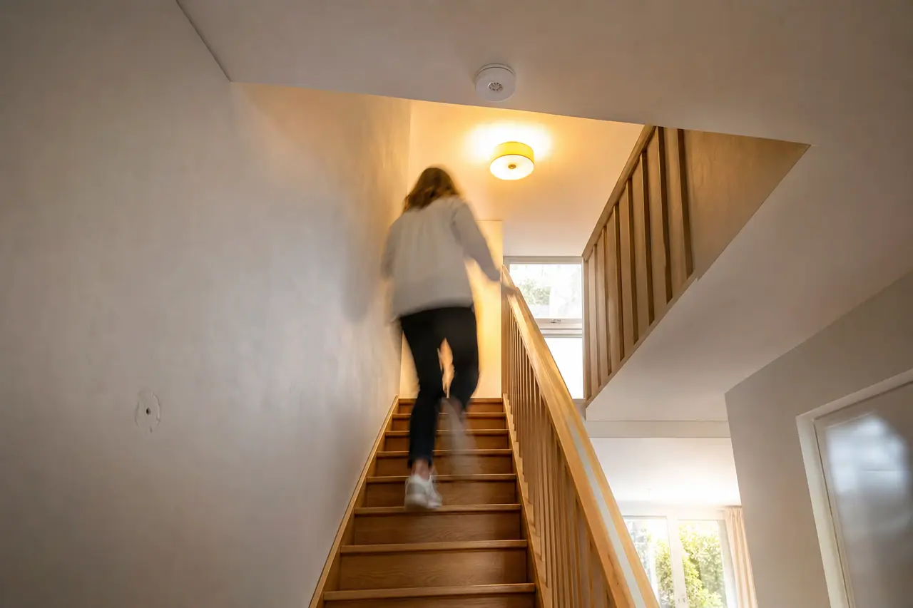 Détecteur de présence blanc fixé au plafond d'une cage d'escalier intérieure éclairée