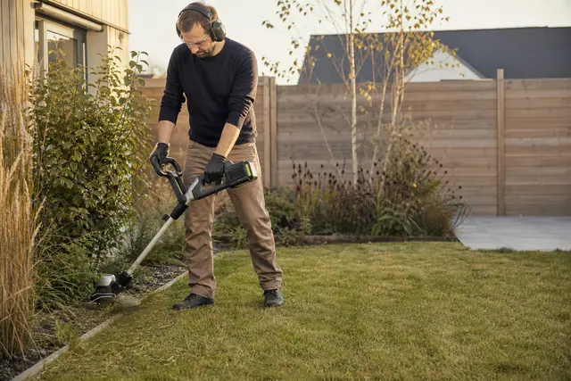 Jardinier équipé utilisant un coupe-bordures sur batterie le long d’une pelouse.