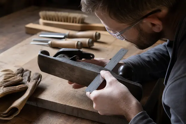 Bricoleur contrôlant la semelle d’un rabot ancien avec une règle métallique.