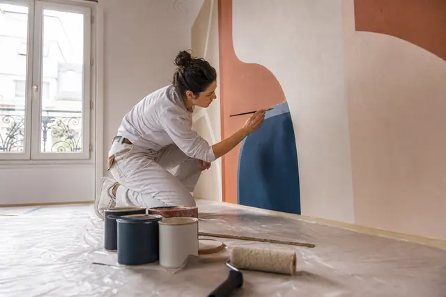 Personne peignant les contours d’une fresque abstraite sur un mur préparé.