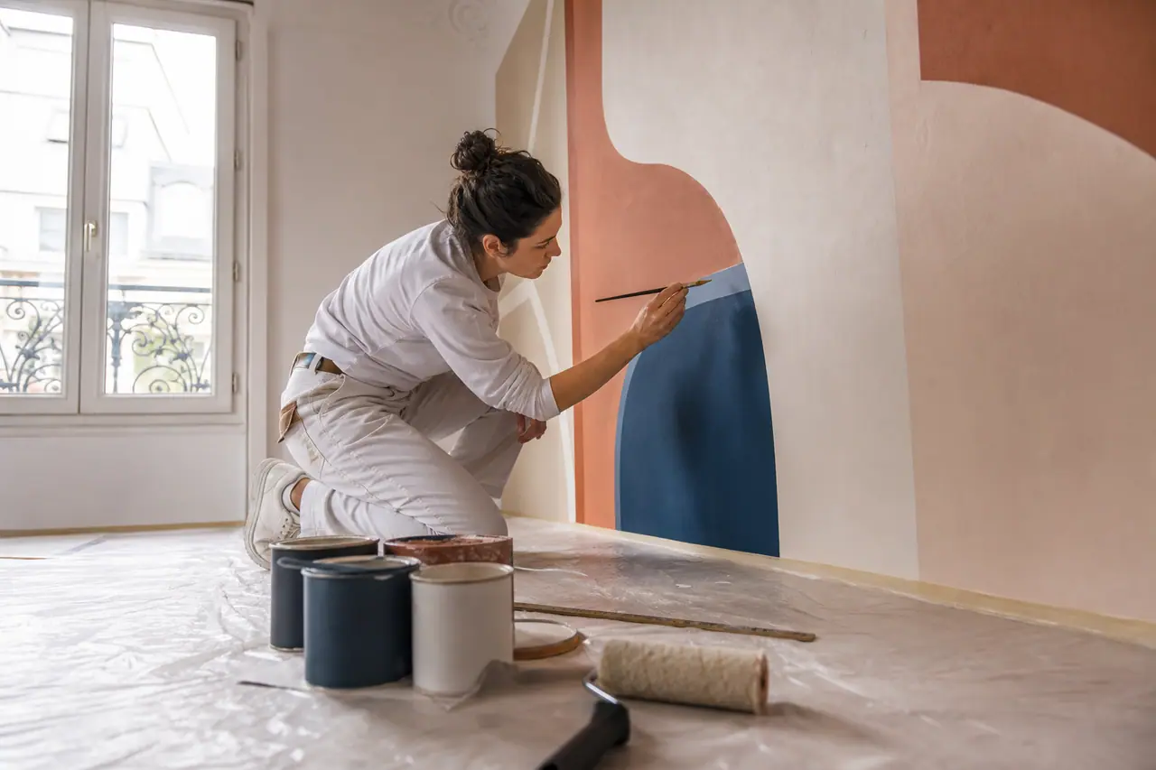 Personne peignant les contours d’une fresque abstraite sur un mur préparé.