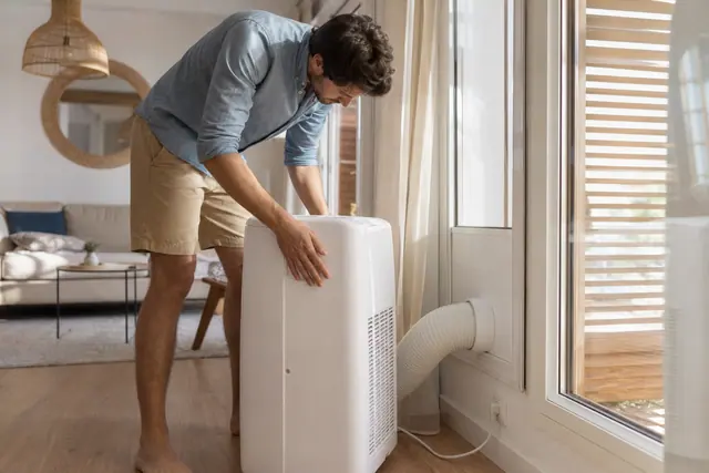 Climatiseur mobile correctement raccordé à une fenêtre étanchée dans un séjour lumineux.