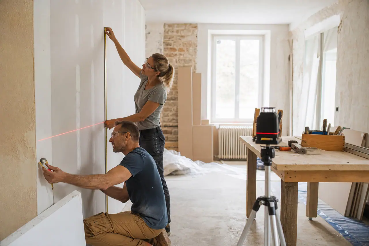 Couple mesurant une cloison pendant la rénovation intérieure sécurisée d’une maison.