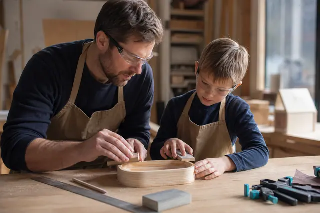 Enfant et adulte ponçant un petit vide-poches en bois sur établi stable.