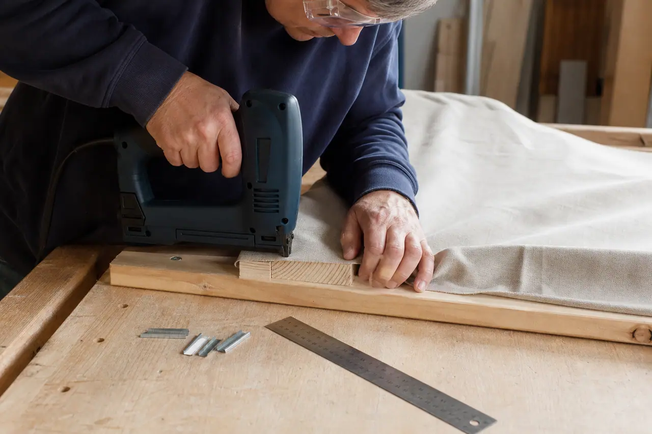 Agrafeuse électrique fixant une toile beige sur tasseau en bois