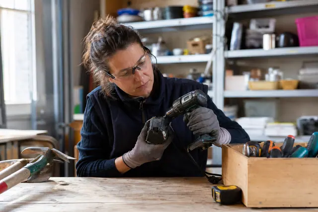 Bricoleuse contrôlant une perceuse d’occasion sur l’établi d’une ressourcerie.