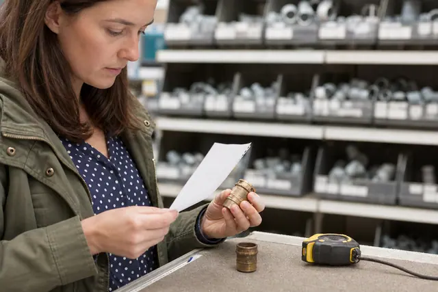 Cliente comparant un raccord de plomberie et ses mesures en magasin.
