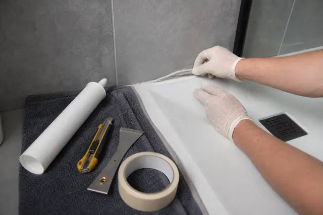 Bricoleur retirant un ancien joint de douche avec outils manuels protégés.