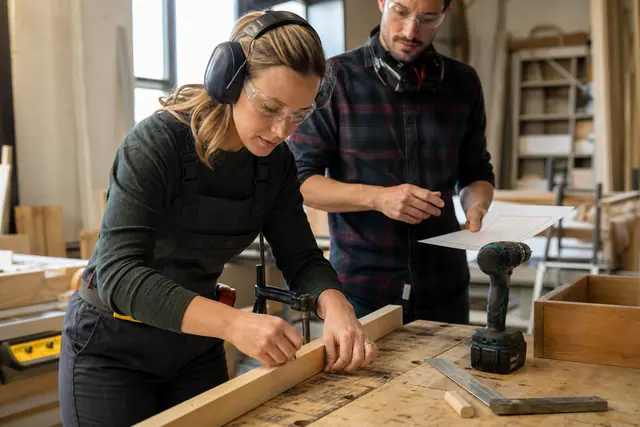 Participant encadré assemblant une pièce de bois sur établi sécurisé.