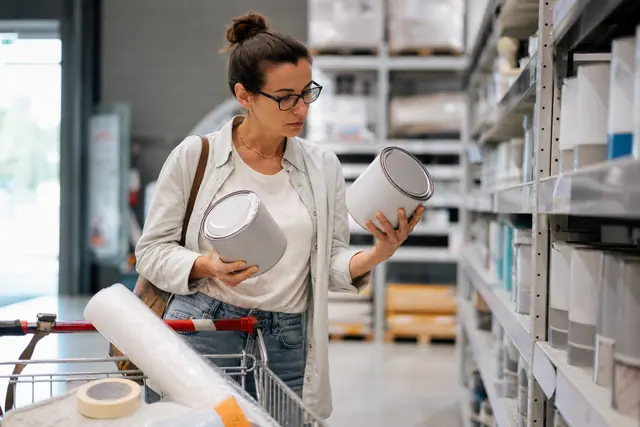Cliente comparant des pots de peinture dans un magasin de bricolage.