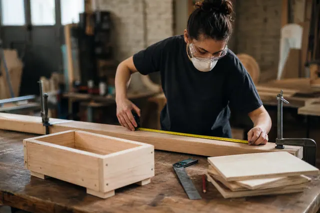 Participant équipé mesurant des planches lors d’un atelier de fabrication