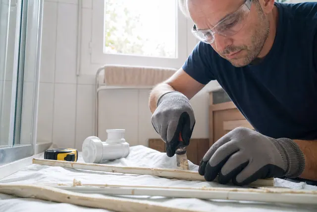 Particulier préparant un joint de douche dans une salle de bains en rénovation.