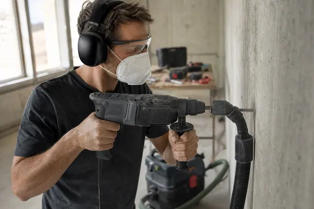 Bricoleur équipé perçant un mur en béton avec perforateur et aspiration.