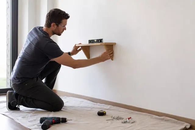 Débutant installant une petite étagère murale avec niveau et protections.