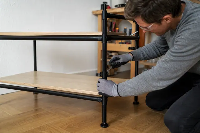 Assemblage d’une étagère en tubes d’acier et tablettes bois dans un salon.