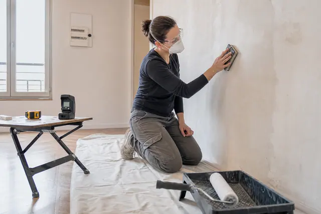 Particulier équipé préparant un mur avant peinture dans un appartement rénové.