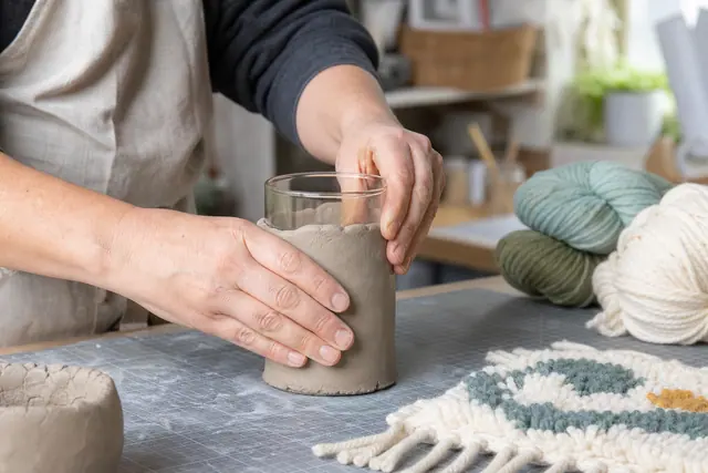 Personne façonnant un cache-vase en argile autour d’un bocal en verre.