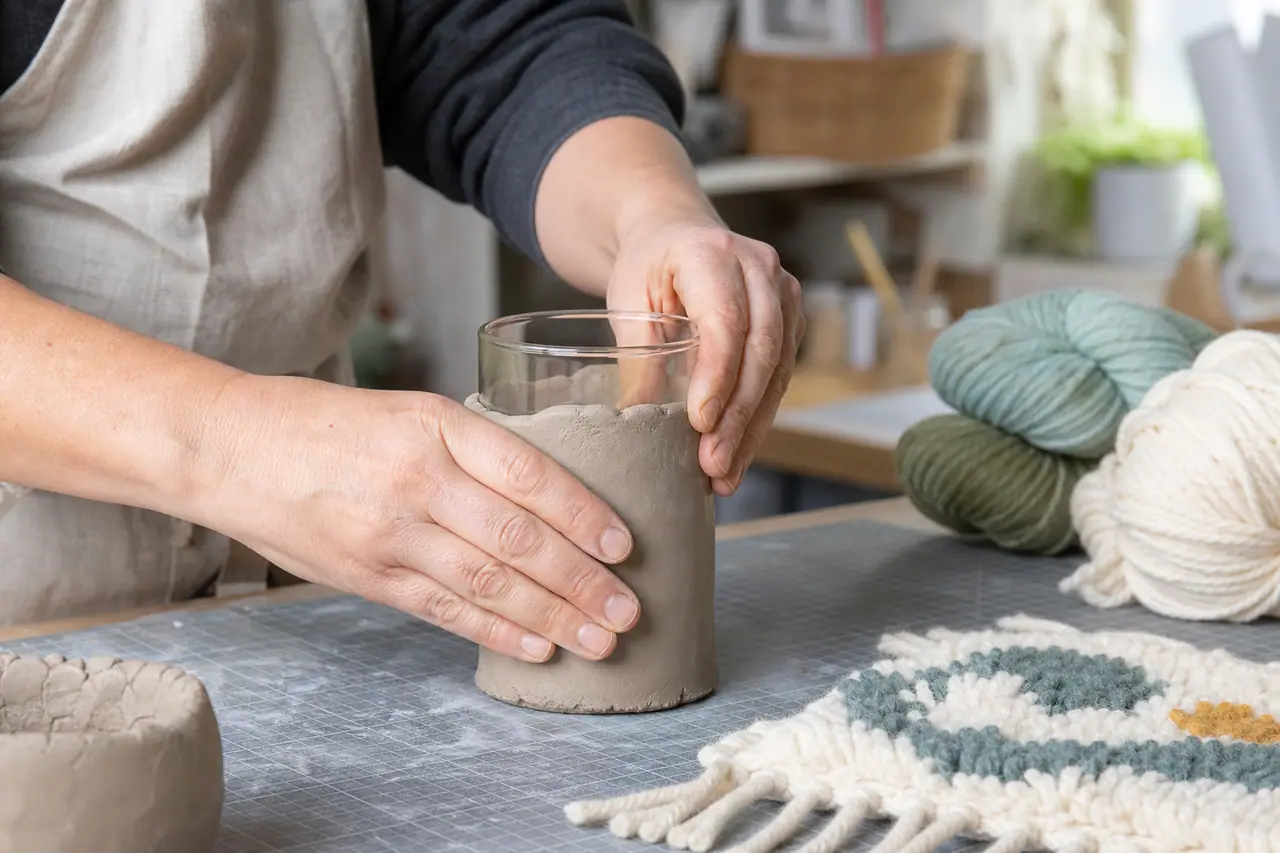 Personne façonnant un cache-vase en argile autour d’un bocal en verre.
