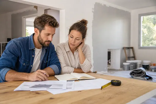 Couple préparant un budget de rénovation autour de devis et outils.