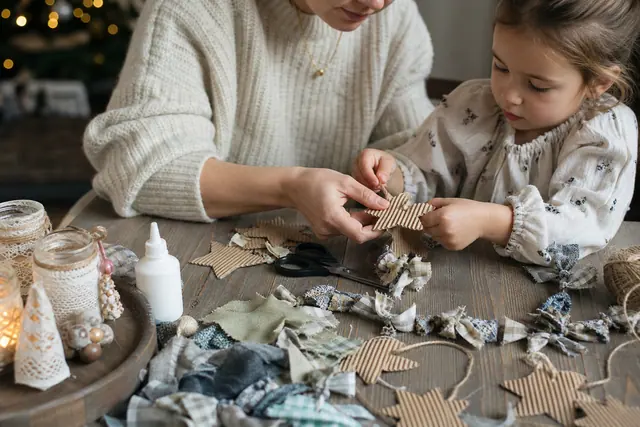 Parent et enfant fabriquant des étoiles en carton recyclé sur une table.