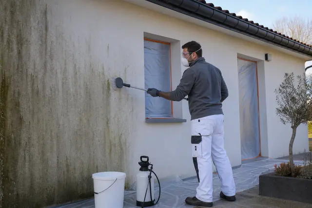 Bricoleur protégé brossant doucement une façade en crépi avant sa rénovation.