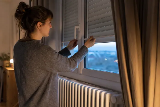 Personne fermant un volet près d’un radiateur dégagé dans un séjour.