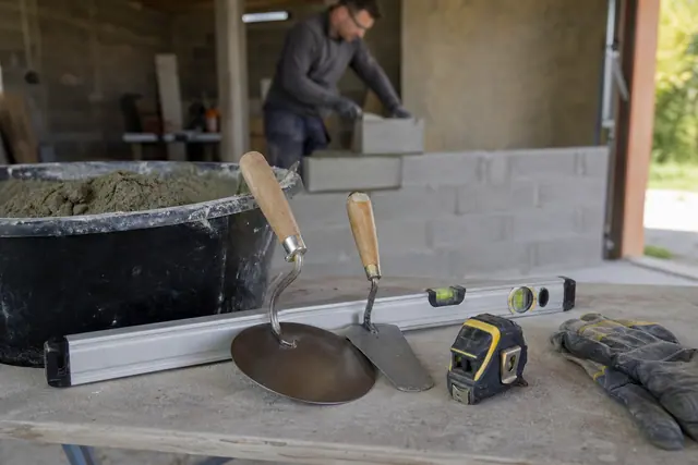 Outils de maçonnerie rangés près d’une auge de mortier sur un chantier domestique.